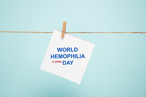 Card with world hemophilia day lettering on rope with pin isolated on blue