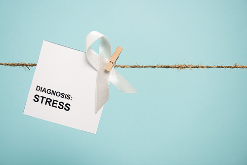 Card with stress diagnosis lettering and white ribbon on rope with pin isolated on blue