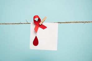 Card with blood drop and red ribbon on rope with pin isolated on blue, concept of hemophilia