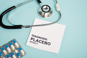 Card with placebo effect lettering, pills and stethoscope on blue background