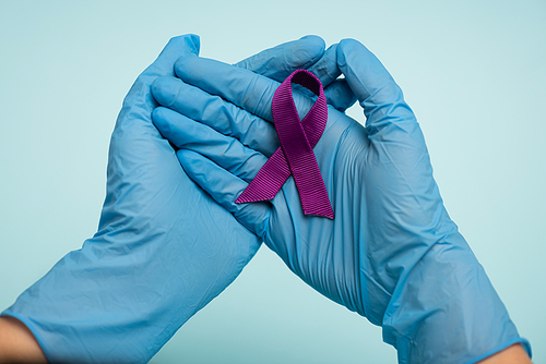 Cropped view of doctor in latex gloves holding purple ribbon isolated on blue