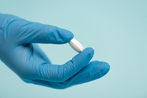 Cropped view of doctor in latex glove holding pill isolated on blue