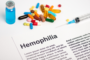 Paper with hemophilia lettering near syringe, vaccine and pills on white background