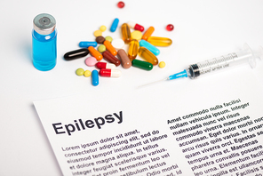 Paper with epilepsy lettering near jar of vaccine, syringe and pills on white background