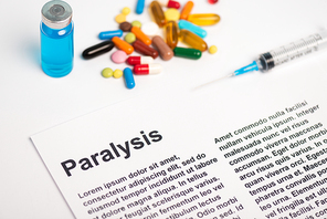 Paper with paralysis lettering near vaccine, syringe and pills on white background