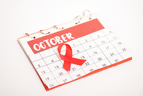 Selective focus of red ribbon of aids awareness on calendar of october isolated on white