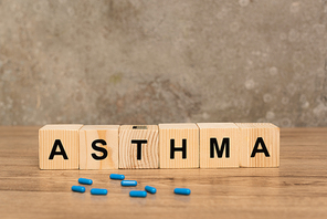 Selective focus of wooden cubes with asthma lettering and pills on wooden table on grey background