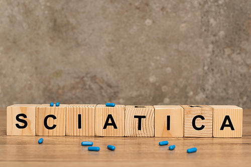 Selective focus of sciatica lettering on cubes with pills on wooden table on grey background