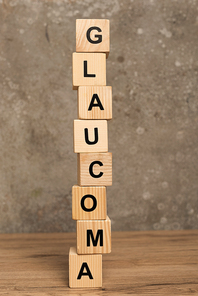 Stacked cubes with glaucoma lettering on wooden table on grey background