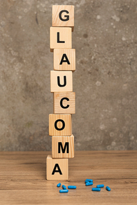 Stacked cubes with glaucoma lettering and pills on wooden table on grey background