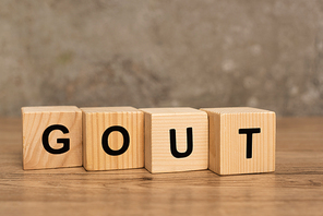 Wooden cubes with gout lettering on wooden table on grey background