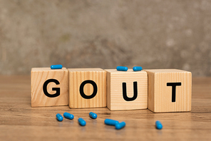 Selective focus of pills on wooden cubes with gout lettering on wooden table on grey background