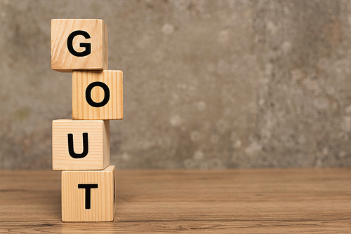 Stacked cubes with gout lettering on wooden table on grey background