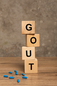 Selective focus of wooden cubes with gout lettering pills on wooden table on grey background
