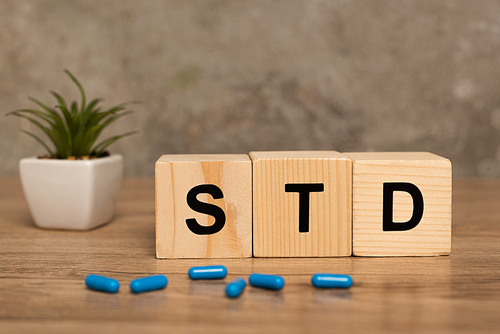 Selective focus of blocks with std letters, pills and plant on wooden table on grey background