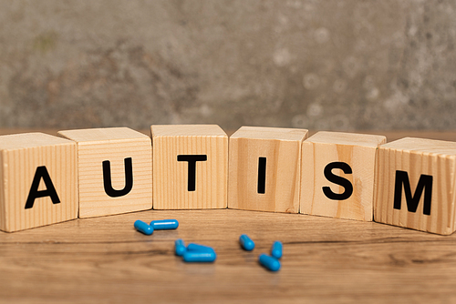 Selective focus of pills and blocks with autism lettering on wooden table on grey background