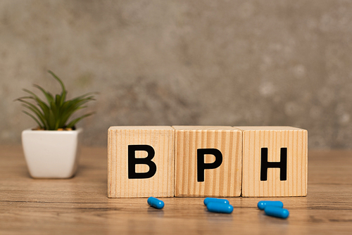 Selective focus of cubes with bph letters and pills with plant on wooden table on grey background