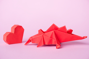 red paper heart near origami dinosaur on pink