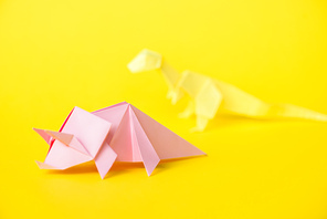 selective focus of pink paper rhinoceros near origami dinosaur on yellow
