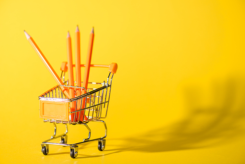 selective focus of toy shopping cart with pencils on yellow