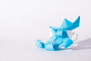cup with paper ship near blue ribbons on white