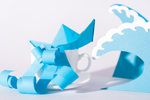 blue paper ship near waves and cup on white