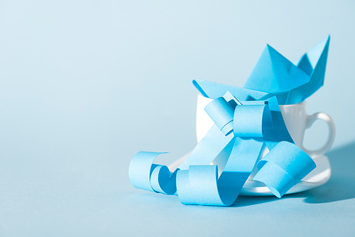 paper ship in white cup near ribbons on blue