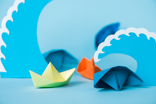 selective focus of colorful paper ships near waves on blue