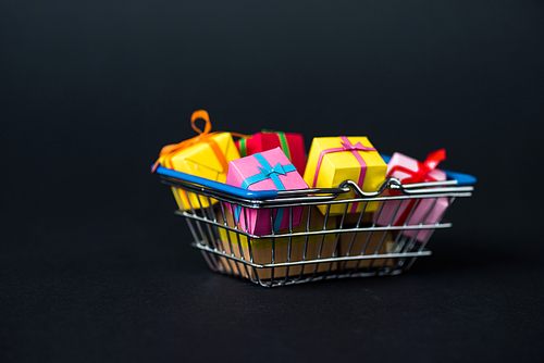 selective focus of colorful gift boxes in shopping basket on black