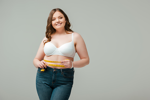 Plus size woman measuring waist,  and smiling isolated on grey