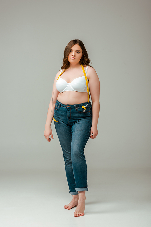 upset plus size woman in jeans and bra standing on grey