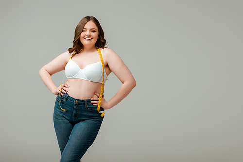 happy plus size woman in jeans and bra standing with hands on hips isolated on grey