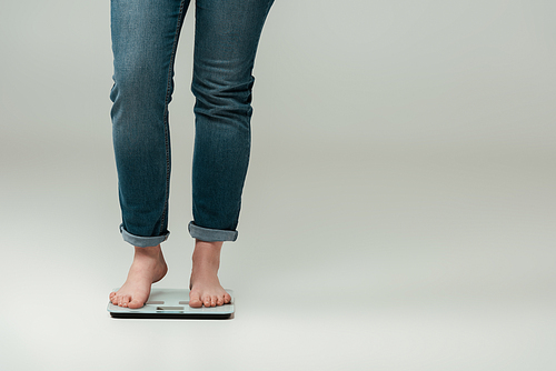 cropped view of plus size girl in jeans standing on scales on grey