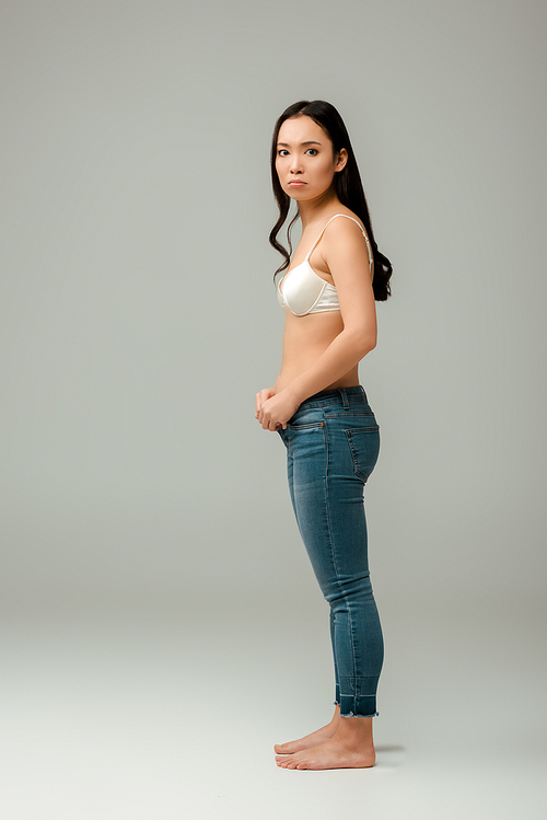 displeased and overweight asian woman wearing jeans on grey