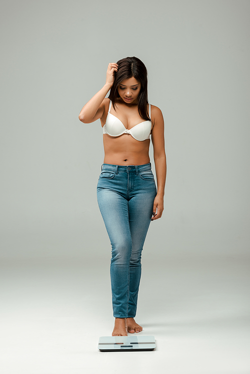 overweight african american girl in jeans and bra looking at scales on grey