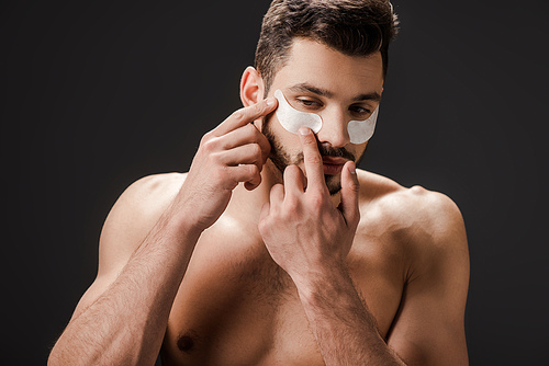 sexy nude man applying eye patches on face isolated on black