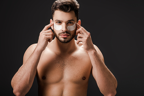 brunette nude man applying eye patches on face isolated on black