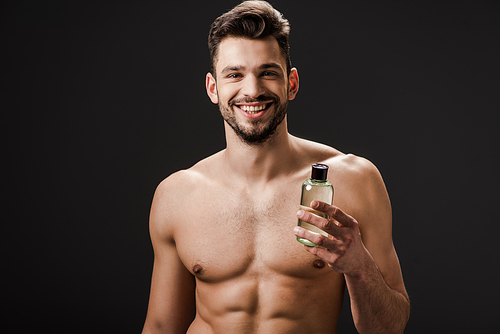 smiling nude man holding bottle of cologne isolated on black