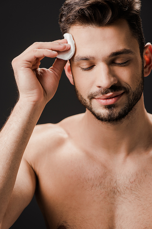 smiling sexy naked man using cosmetic cotton pad isolated on black
