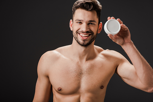 smiling nude man holding plastic container with face cream isolated on grey