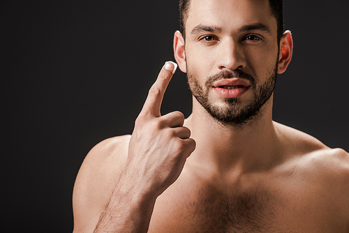 handsome naked man applying face cream isolated on black