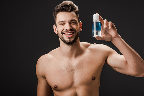 smiling sexy nude man holding bottle with cosmetic liquid isolated on black