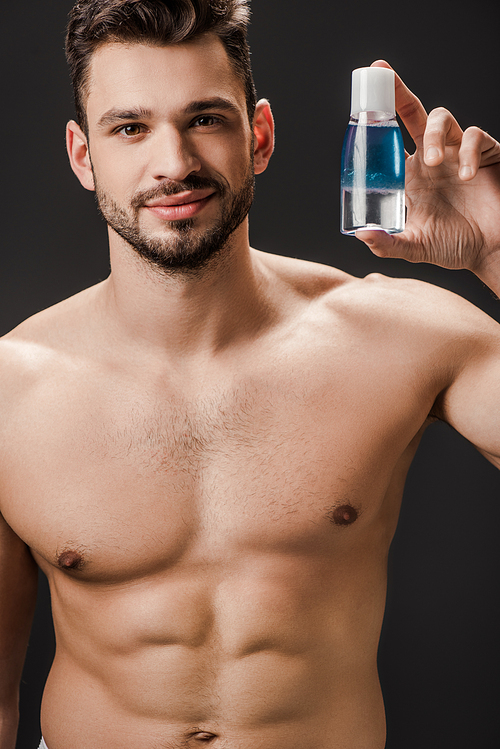 sexy bearded naked man holding bottle with cosmetic liquid isolated on black