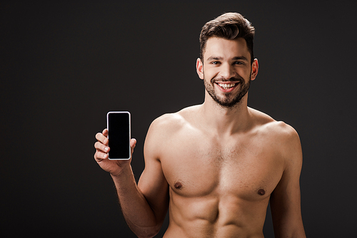 smiling sexy naked man showing smartphone with blank screen isolated on black
