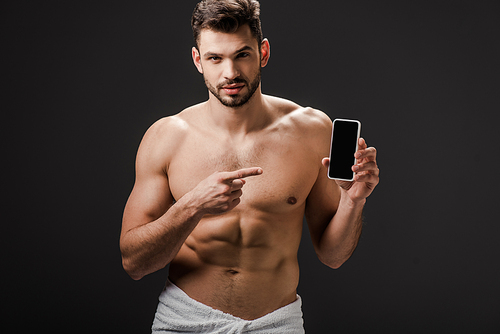 sexy man in towel pointing at smartphone with blank screen isolated on grey
