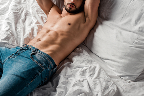 cropped view of sexy shirtless man in jeans lying on bed