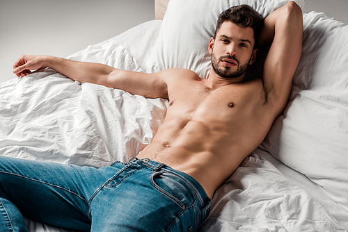 handsome sexy shirtless man in jeans lying on bed on grey