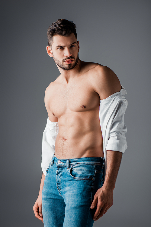 brunette sexy man in white shirt and jeans isolated on grey