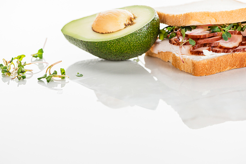 fresh delicious sandwich with meat and sprouts on white surface near avocado