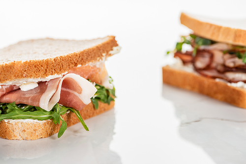 selective focus of fresh sandwich with arugula and prosciutto on marble white surface